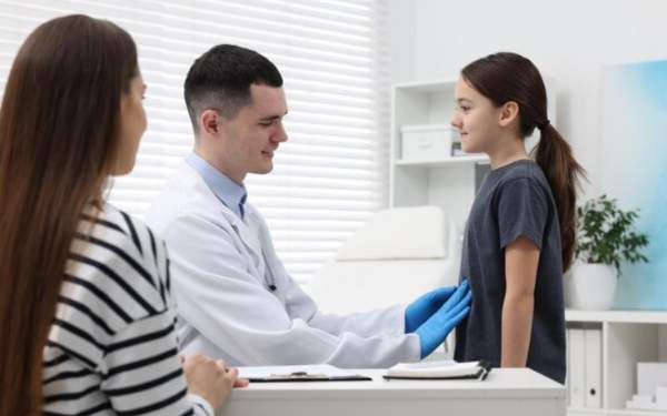 Niña en consulta médica con su mamá y un pediatra, ilustrando la importancia de acudir al especialista por pubertad temprana.