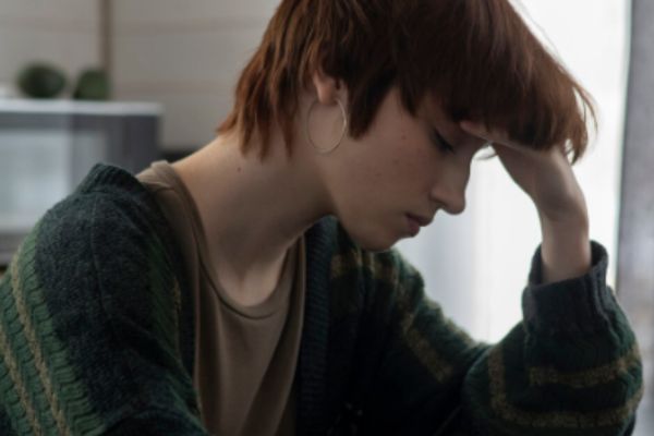 Adolescente con expresión triste y aislada de otras personas, reflejando soledad y baja autoestima.