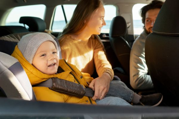 Bebé feliz con arnés ajustado y ropa cómoda en su silla de auto durante un viaje largo con su familia.
