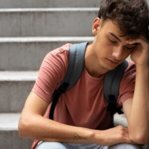 Adolescente triste sentado en unas escaleras con expresión de inseguridad y baja autoestima.
