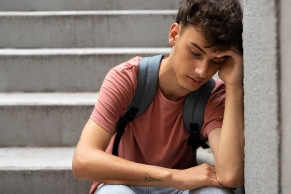 Adolescente triste sentado en unas escaleras con expresión de inseguridad y baja autoestima.