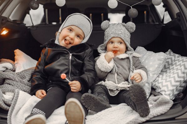 Niños cómodos en cajuela con organizadores de ropa, snacks e higiene para un viaje largo en auto con bebé.