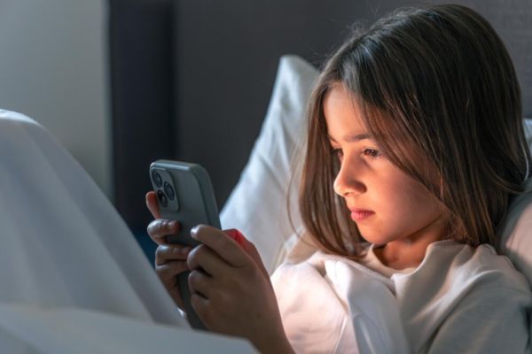 Adolescente usando el celular en su cama antes de dormir.